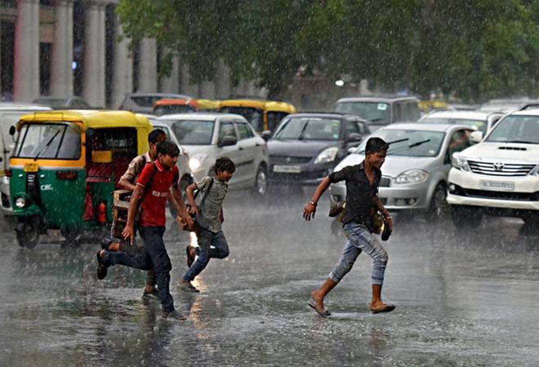 People crossing a wet and busy road in rain near Connaught Place in Delhi